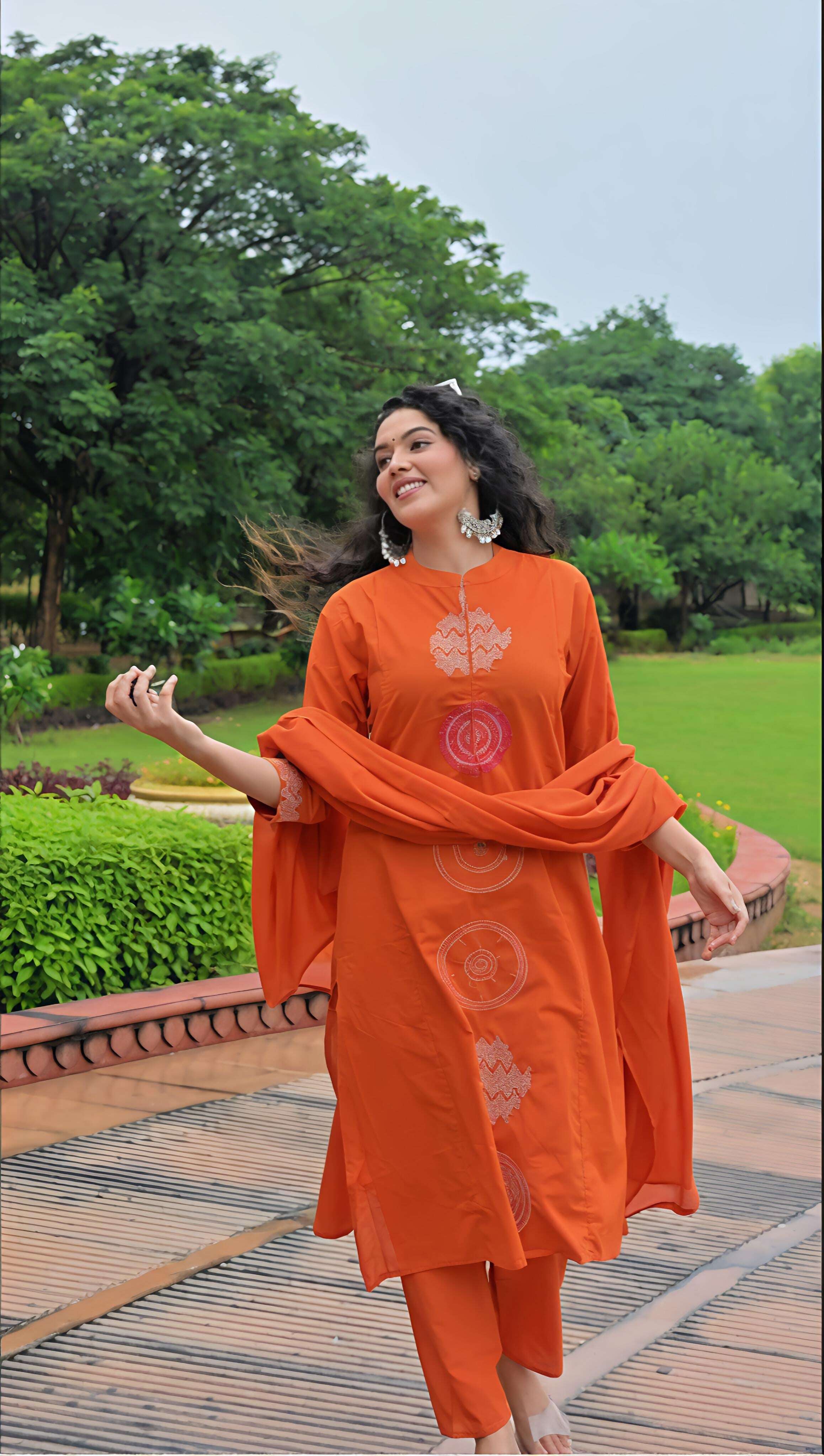 Woman wearing an orange cotton kurta set with beautiful embroidery in a lush garden setting