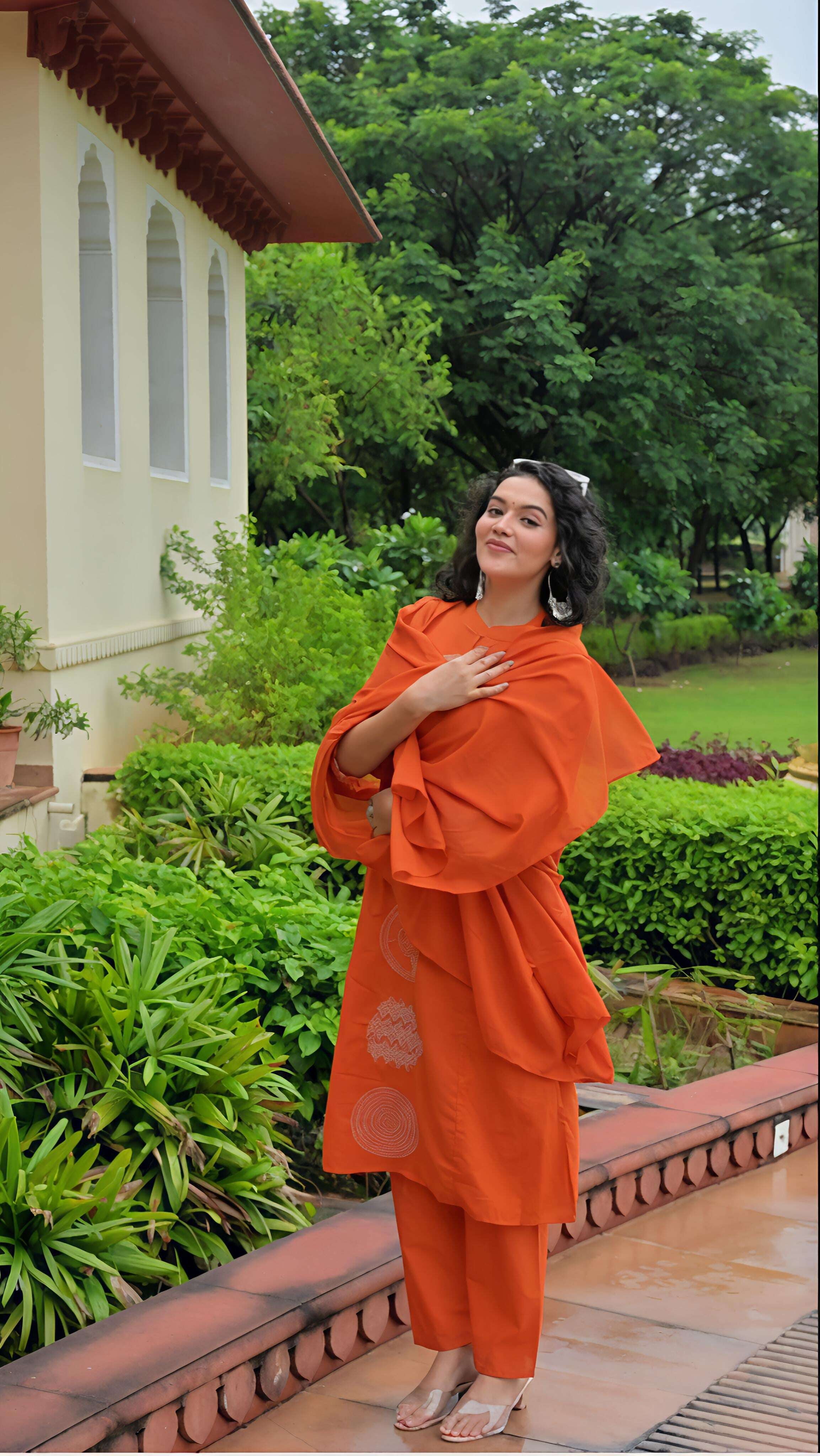 Elegant woman wearing an orange cotton kurta set with matching pants in a lush garden setting